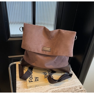 Close-up of brown suede tote bag with leather trim and wide strap on stone surface