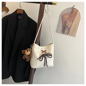 Detail of a beige canvas bucket bag featuring a blue striped bow and plush bear charm