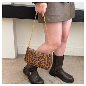 Detail of leopard print handbag featuring a gold chain strap held by a model