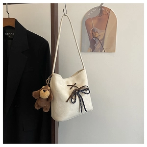 Detail of cream suede bucket bag with ribbon bow and brown puppy plush pendant