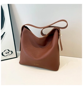 Close-up of brown leather hobo bag showing matte grain texture and wide shoulder strap