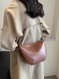 Chic brown crescent leather bucket bag for women worn over a stylish trench coat