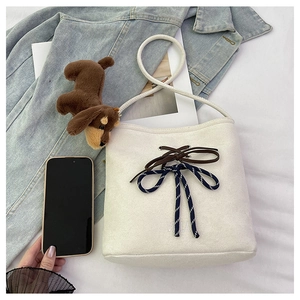 Detail of white suede bucket bag featuring striped bow and cute brown puppy plush charm