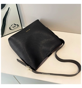 Detail of minimalist black bucket bag featuring golden twist lock and textured matte leather