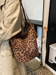 Leopard print bucket bag with brown leather straps shown on shoulder in a warm indoor setting