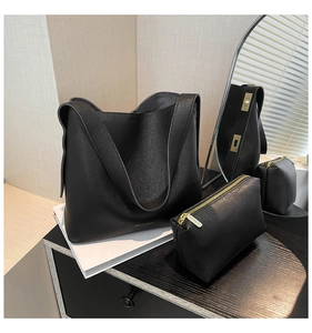 Detail of black tote bag set with textured leather and inner pouch on reflective surface