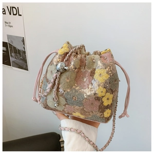 Dettaglio borsa a secchiello con paillettes floreali e tracolla a catena intrecciata rosa