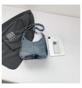 Detail of light blue denim hobo bag with adjustable strap on white minimalist desk