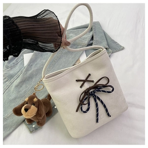 Detail of cream canvas bucket bag with lace-up bow design and plush puppy charm