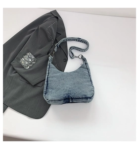 Detail of blue denim hobo bag with adjustable strap on a minimalist white surface