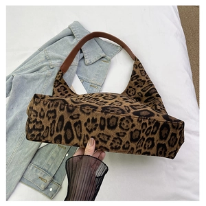 Detail view of the vintage leopard print tote with brown leather straps on a soft bed