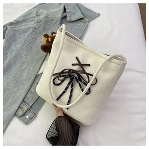 Detail of cream canvas bucket bag with layered bow design and cute plush bear charm