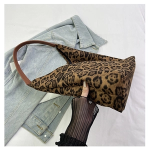 Close-up of leopard print tote bag with brown leather strap and denim jacket accent
