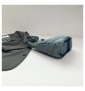 Detail of blue denim shoulder bag showing texture, silver metal hardware and wide strap