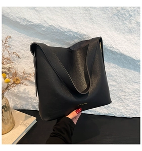 Detail of matte black minimalist bucket bag featuring a gold logo and wide strap