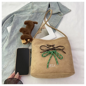 Brown suede bucket bag with decorative bow and plush puppy charm on a styled background