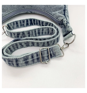 Detailed shot of adjustable denim strap and silver metal hardware on a blue handbag