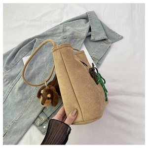 Close-up of brown suede bucket bag featuring green woven knot and dachshund plush charm