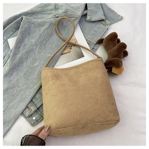 Detail of light brown suede bucket bag with slim shoulder strap on casual denim background