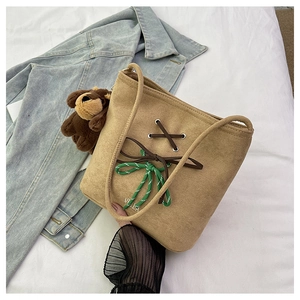 Detail of khaki suede bucket bag with decorative cross-lacing and cute bear charm