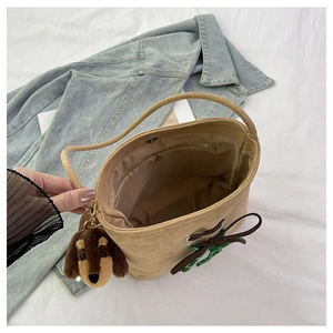 Detail of light brown suede bucket bag featuring a plush dog charm and bow tie detail