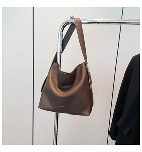 Close-up of brown leather hobo bag with wide shoulder strap and gold brand lettering