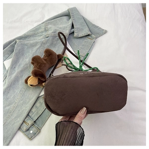 Detail of dark brown suede bucket bag featuring a plush dog charm and green woven handle