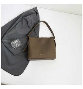 Detail of dark brown leather bucket bag with gold logo on a clean white surface