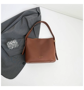 Flat lay of brown leather tote bag with wide strap and gold logo detail on white background