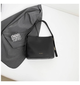Detailed macro view of minimalist black leather shoulder bag with gold hardware and branding