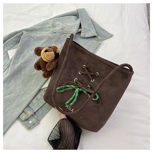 Detail of brown suede bucket bag with green knotted accents and plush bear charm
