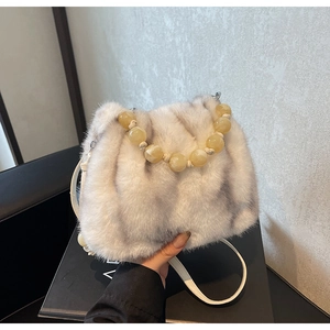 Detail of faux mink bucket bag featuring amber bead handle and white crossbody strap