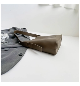 Detail of coffee brown leather bucket bag with wide shoulder strap on a white surface