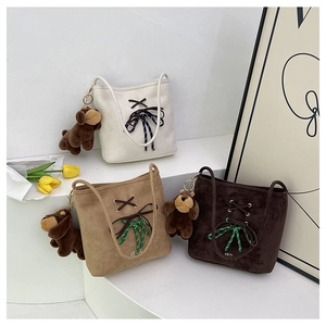Three suede bucket bags in white, khaki, and brown with cute plush bear charms on display