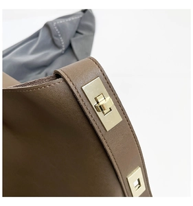 Close-up of golden turn-lock closure on brown leather bucket bag with metallic texture