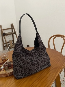 Vintage leopard print canvas tote bag with black leather straps on a wooden table