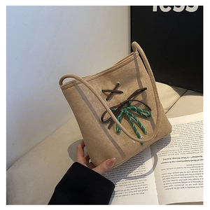 Detail of khaki suede shoulder bag featuring brown cross-laces and green bow accent