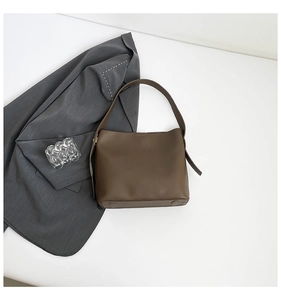 Detail view of large dark brown leather bucket bag with wide strap and polished texture