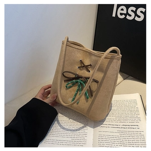 Close-up of beige suede bucket bag featuring leather cross-ties and woven bow detail