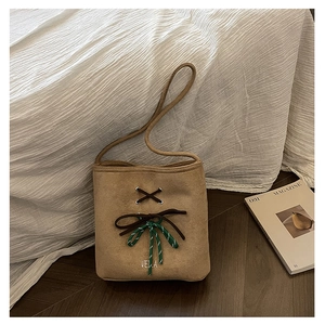 Detail of light brown suede bucket bag with woven bow and leather tie on wood floor
