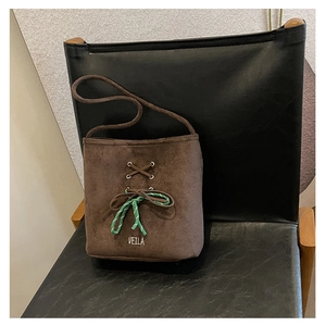Close-up of brown suede bucket bag featuring cross-lace detail and green woven cord on a chair