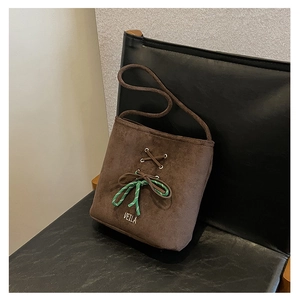 Macro detail of brown suede bucket bag featuring leather cross-stitching and woven knot