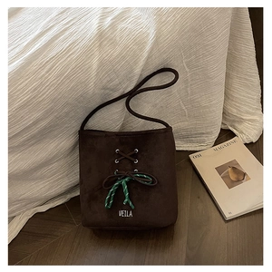 Close-up of dark brown suede bucket bag featuring woven bow detail and logo on wood floor