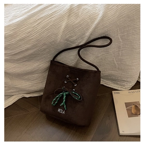 Close-up of brown suede bucket bag featuring cross lacing and a striped knot detail