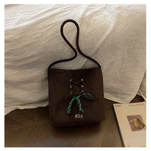 Close-up of brown suede bucket bag featuring cross-lace design and woven bow detail