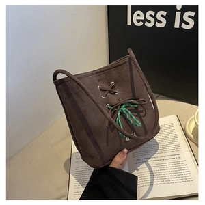 Detail view of coffee suede bucket bag with green woven rope and cross-tie design