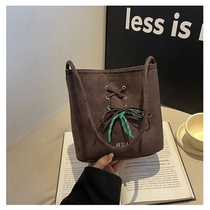 Detail of dark brown suede bucket bag featuring woven ribbon and metal eyelet lacing