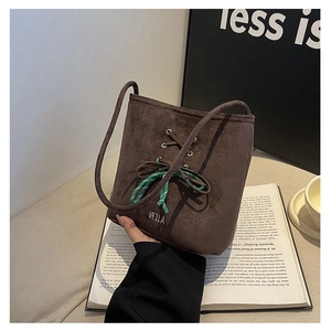 Detail of dark brown suede bucket bag with lace-up design and woven bow accent