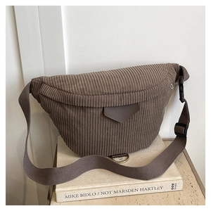 Detailed close-up of dark brown corduroy belt bag with adjustable strap on white book