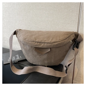 Detail of brown corduroy crossbody bag texture with shield-shaped leather patch and strap